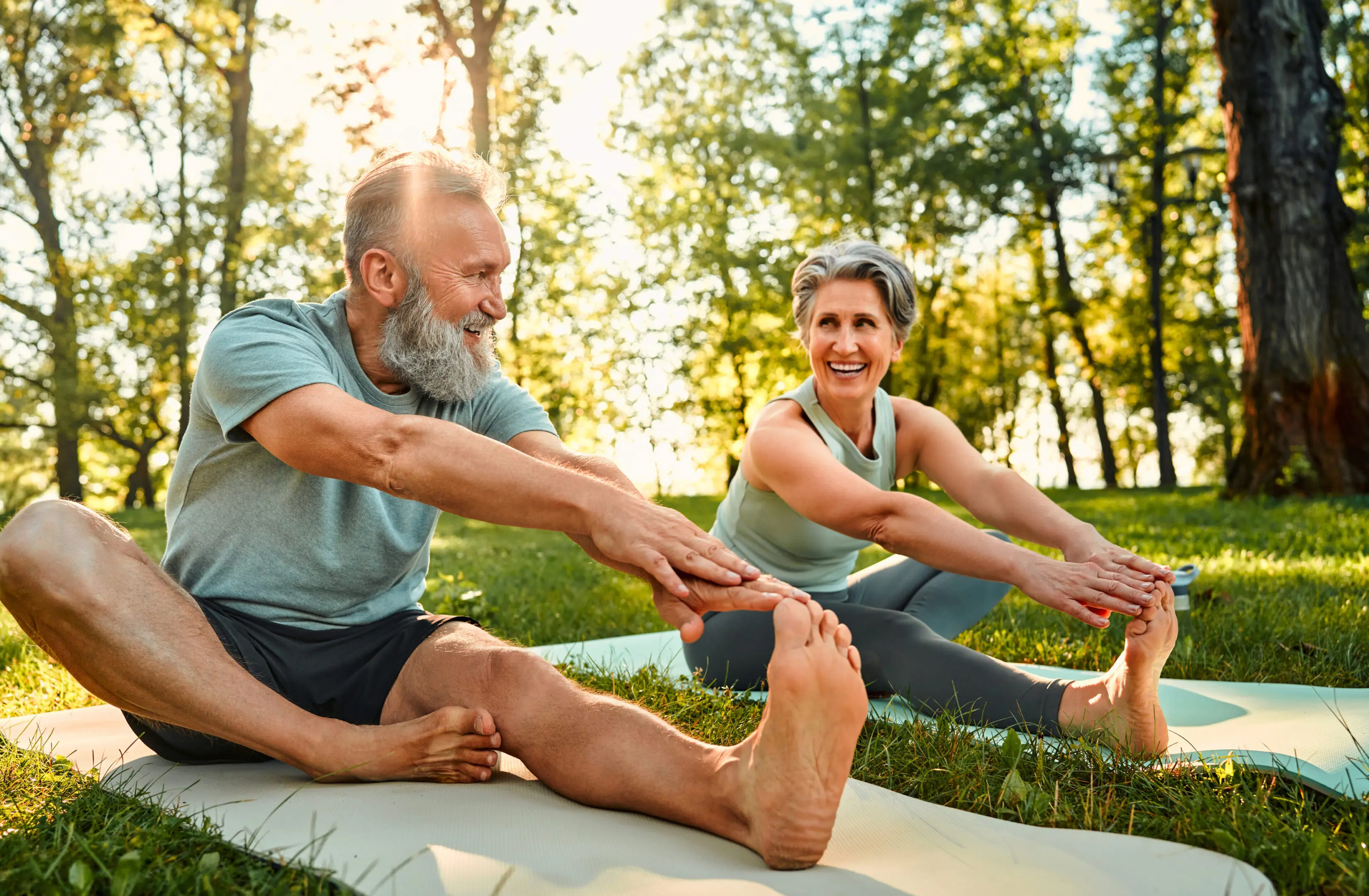 Older couple stretching on yoga mats outdoors.
