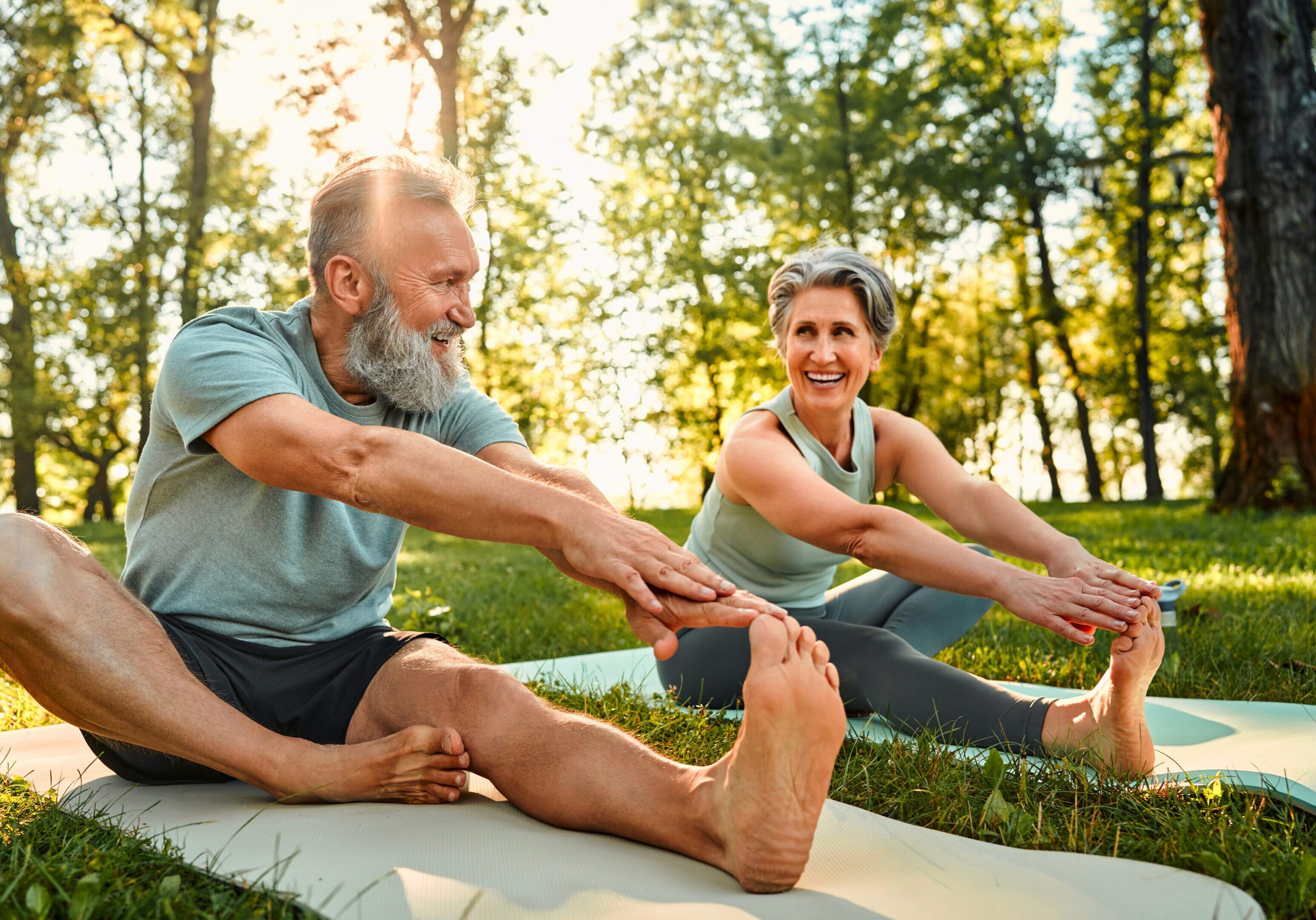 Older couple stretching on yoga mats outdoors.